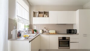 Une cuisine moderne avec des meubles blancs, un four encastré et un four à micro-ondes. Une fenêtre offre une vue sur l’extérieur, et une plante est posée sur le plan de travail.