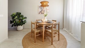 Un coin repas avec une table ronde, des chaises en osier, un tapis en fibres naturelles, un luminaire suspendu, une plante en pot et des œuvres d’art encadrées accrochées au mur.