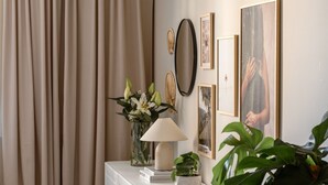 Une pièce bien éclairée, avec un meuble blanc, une lampe, un vase de fleurs et des tableaux encadrés accrochés au mur.