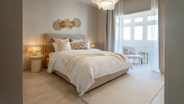 Une chambre moderne avec un grand lit, des lampes de chevet, un élément décoratif mural et une vue sur l’extérieur à travers des rideaux légers.