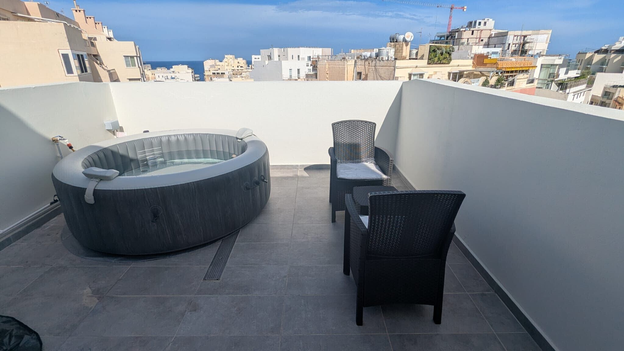 Une terrasse sur le toit avec un jacuzzi, deux fauteuils en osier et une vue sur le paysage urbain.