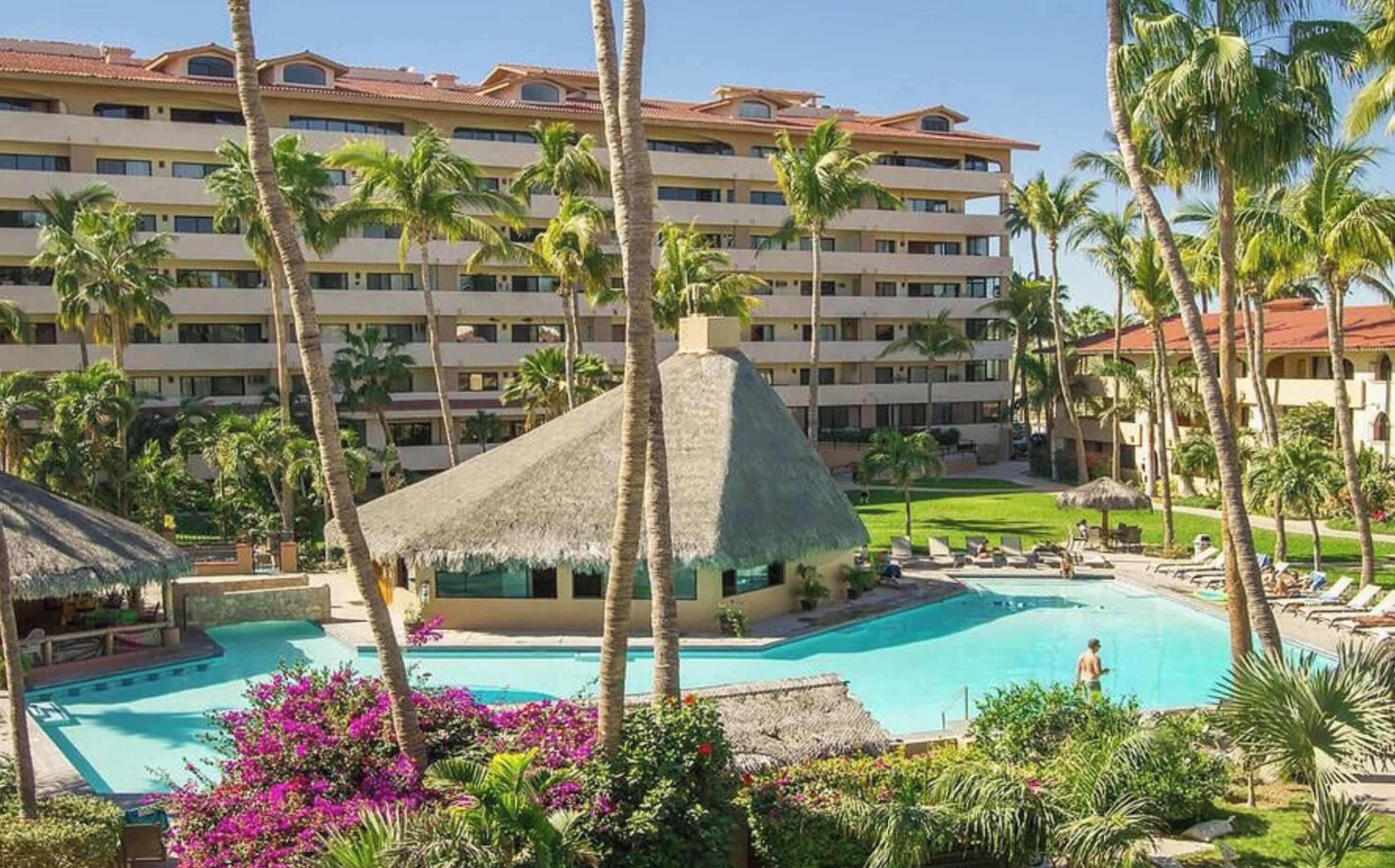 Un resort con una piscina grande, palmeras y un edificio con varios balcones.