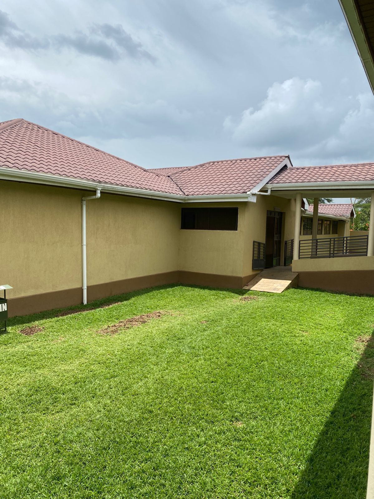 A building with a flat roof, a covered walkway, and a grassy courtyard.