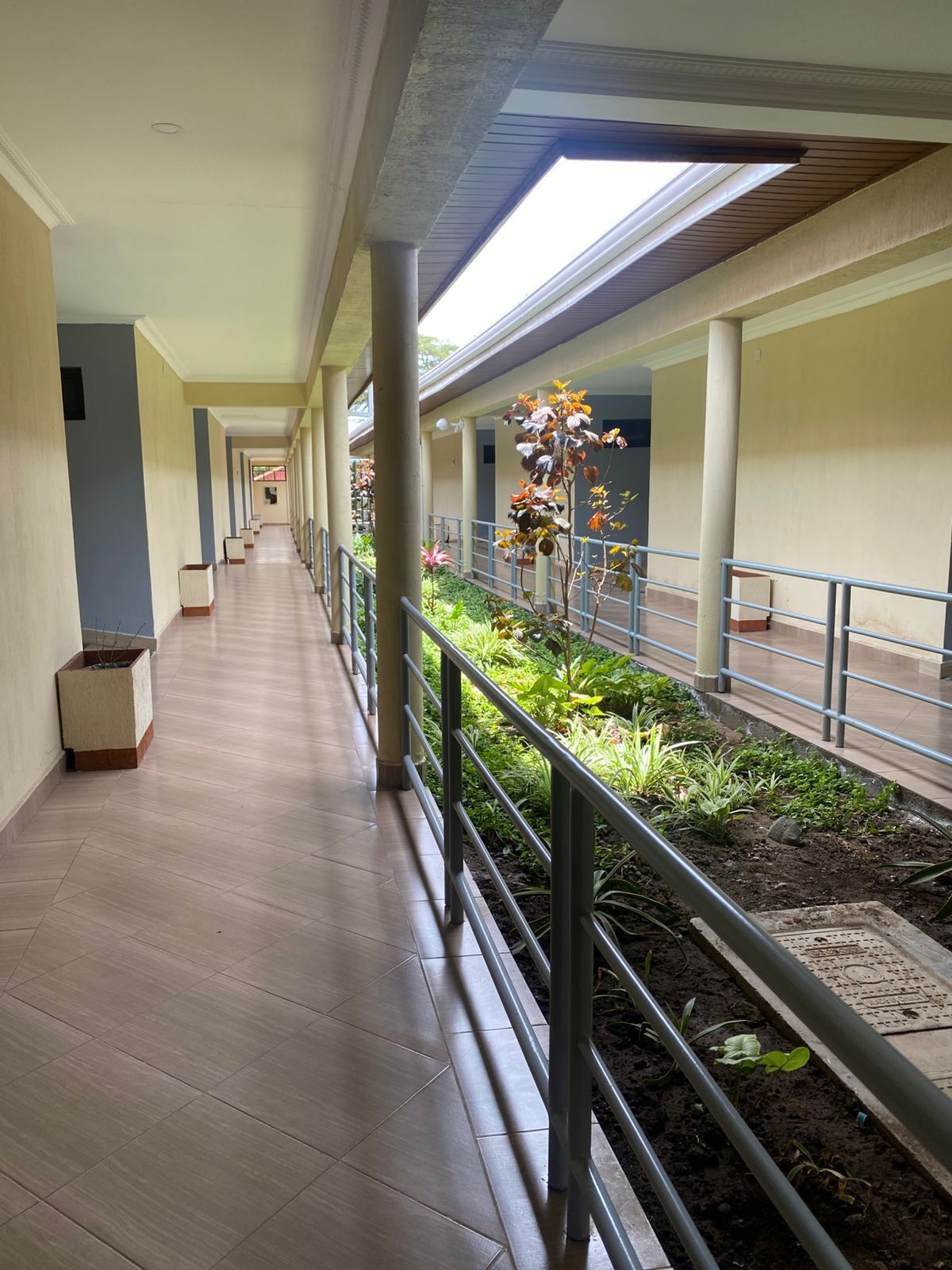 A corridor with a tiled floor, metal railings, and a garden area with plants and flowers.