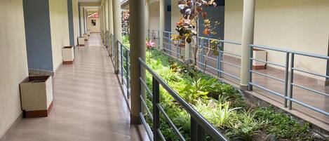 A corridor with a tiled floor, metal railings, and a garden area with plants and flowers.