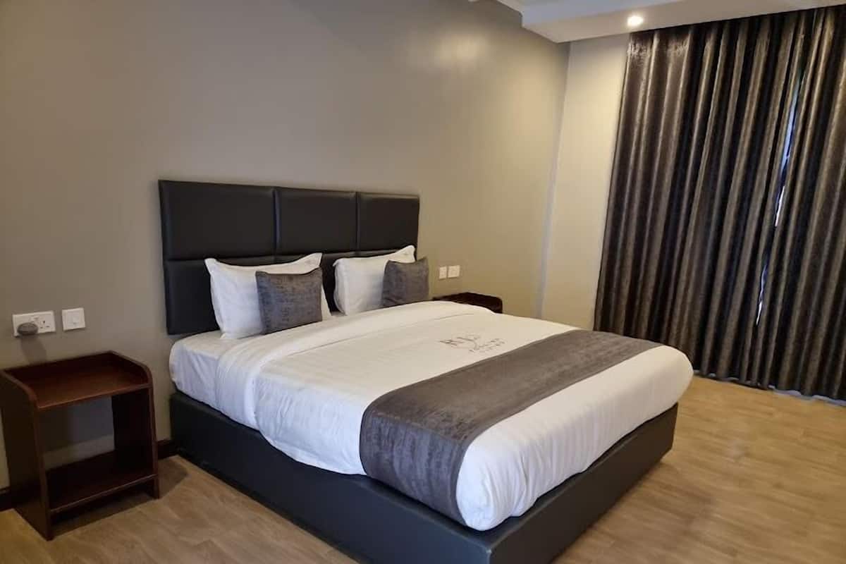 A modern hotel room with a large bed, dark headboard, and a wooden nightstand.