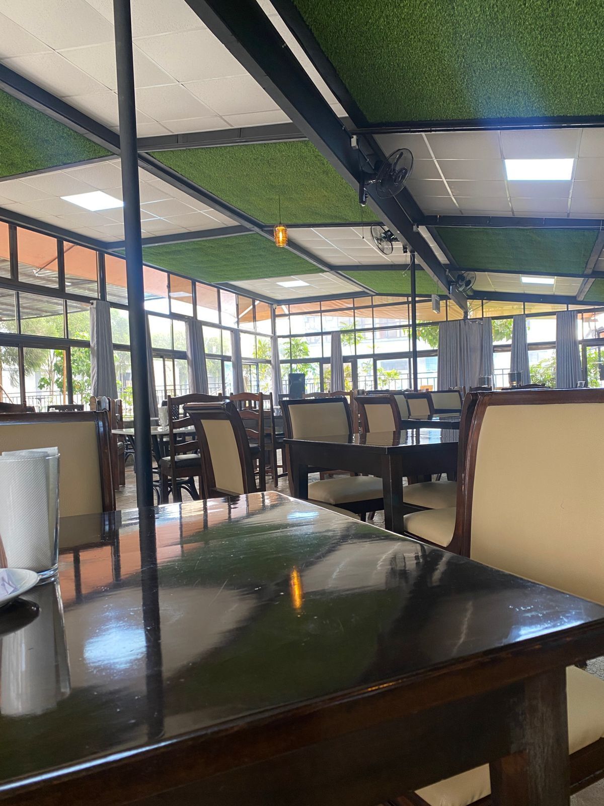 Un restaurant avec de hauts plafonds, un revêtement de sol en gazon synthétique vert et de grandes fenêtres. Les tables sont disposées pour accueillir les clients.