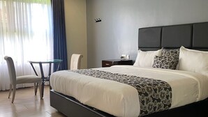 Ein Hotelzimmer mit einem großen Bett, einem Sessel, einem kleinen Tisch und einem Nachttisch.