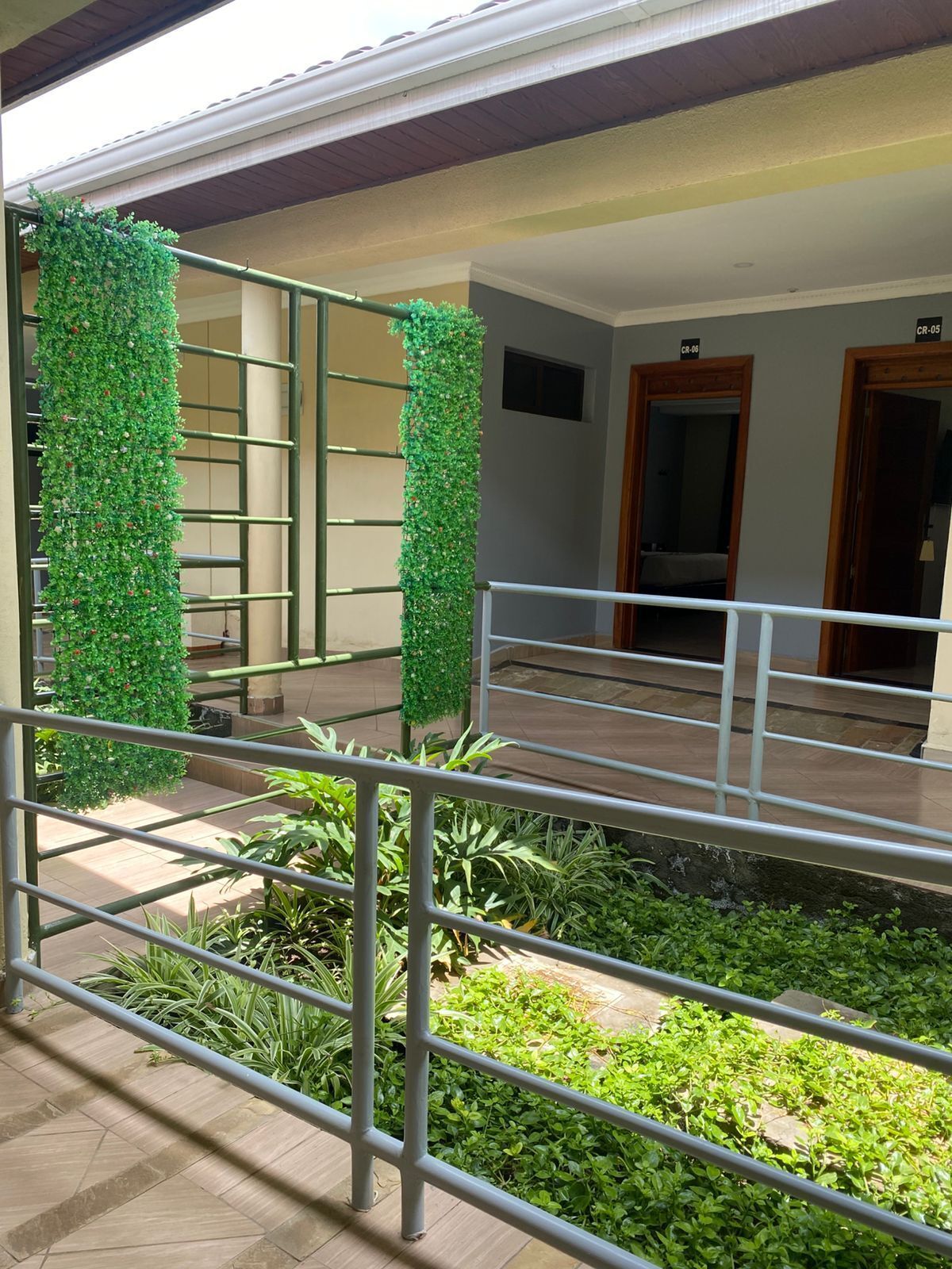 Un pasillo de hotel con barandilla de metal, plantas artificiales verdes y suelo de baldosas.