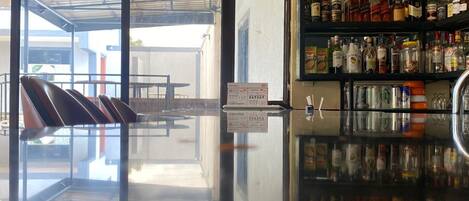Una zona de bar con suelo pulido que refleja el interior, una barra y estantes llenos de diferentes botellas.
