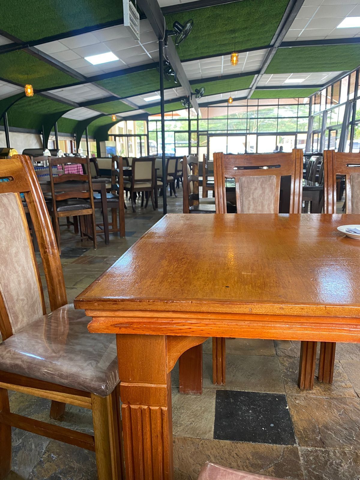 Un restaurante con una gran mesa de madera, sillas y un techo alto cubierto de césped artificial.