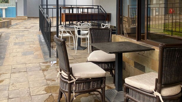 Eine Terrasse im Freien mit Steinboden, Korbmöbeln und einer überdachten Sitzgelegenheit.