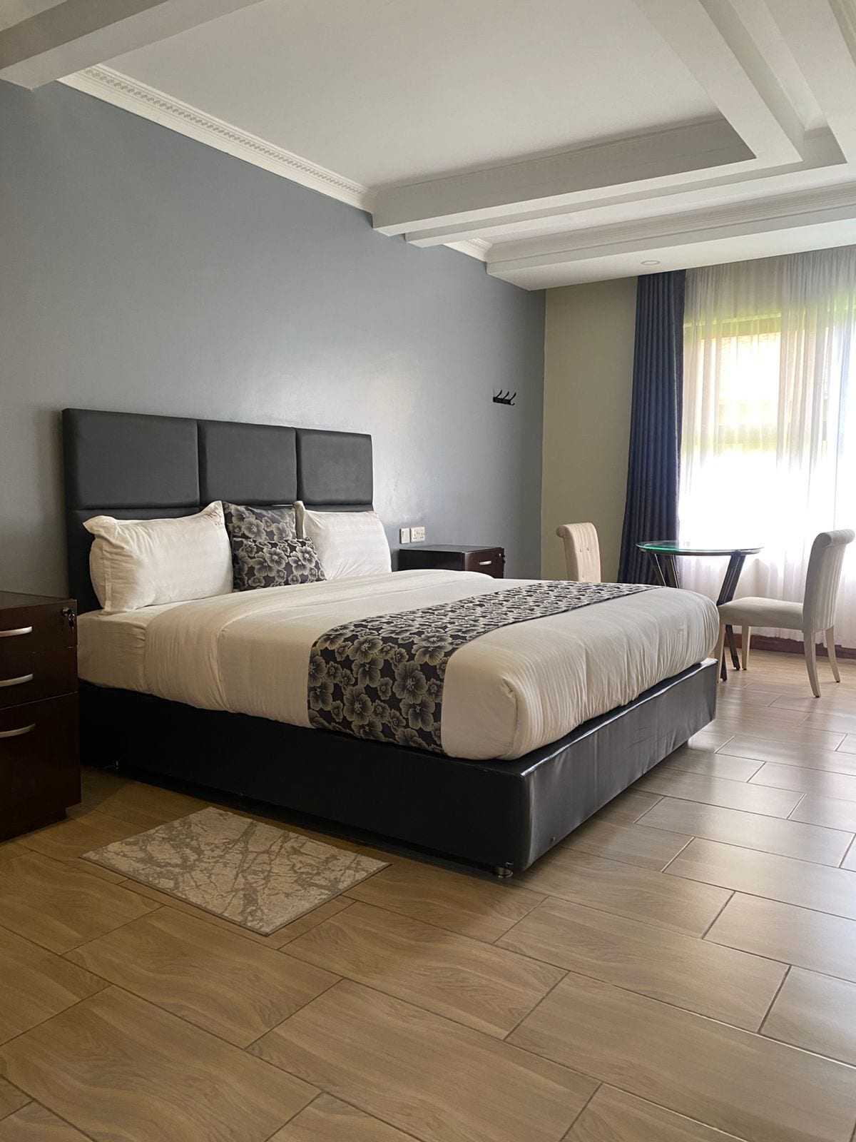 A modern hotel room with a large bed, a desk, a chair, and a small table.