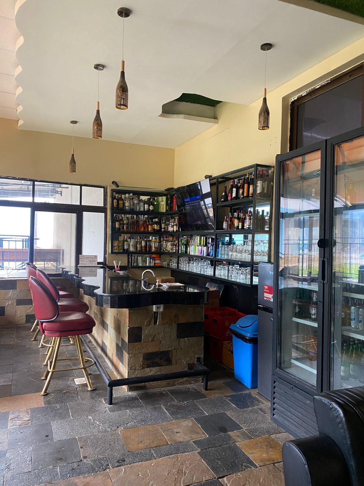 Zona de bar amb un taulell de pedra, tamborets vermells i una vitrina de vidre.