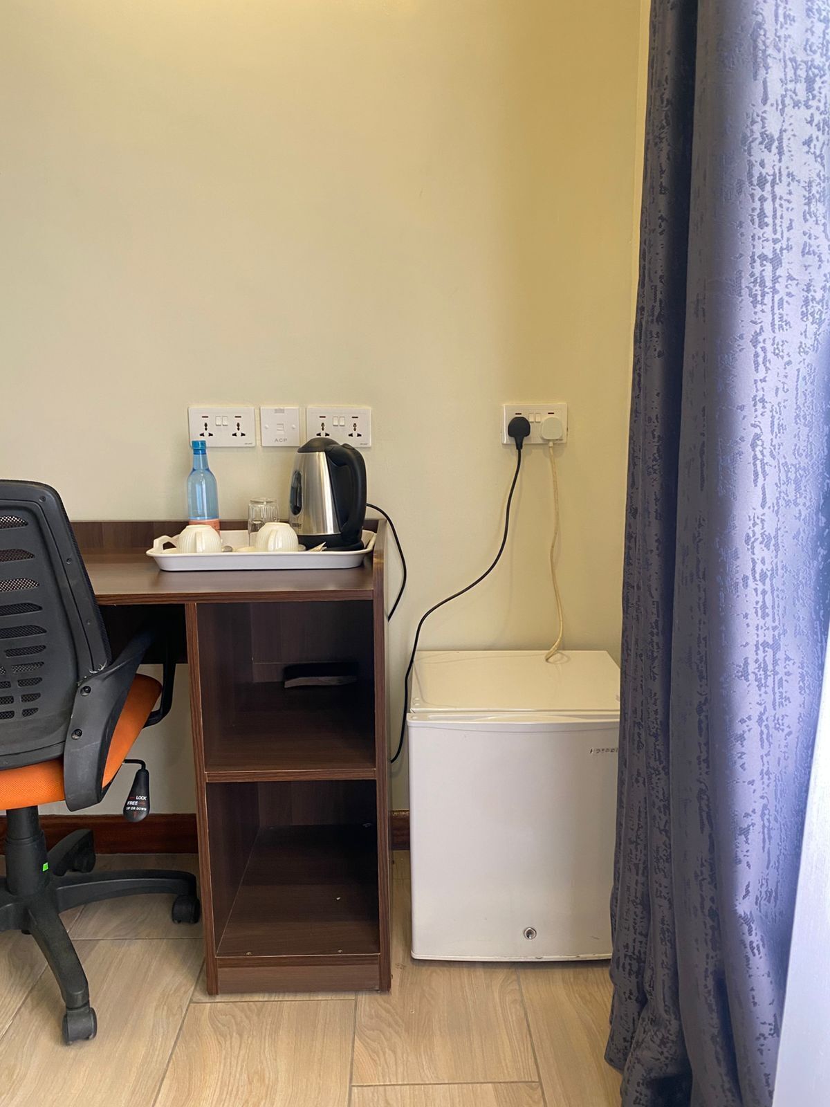 A small office space with a desk, chair, kettle, kettle pot, and a white storage unit.