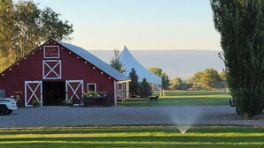 A red barn with a white cross truss roof, a white truck parked in front, and a clear view of the surrounding landscape.