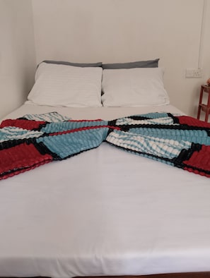 Un lit avec un matelas blanc, deux oreillers blancs et une couverture colorée.