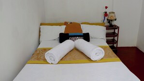 Ein ordentlich gemachtes Bett mit weißen Leinen, einem braunen Kopfkissen und zwei aufgerollten Handtüchern.