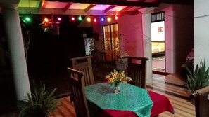 Un área de comedor al aire libre con una mesa cubierta con mantel verde, sillas de madera y plantas en macetas.