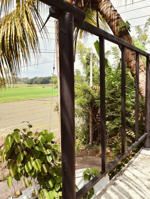 A metal railing with a view of a green field and a palm tree.