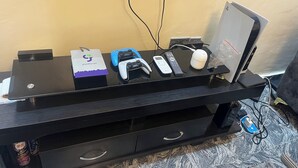 A gaming setup with a monitor, two game controllers, a mouse, and a remote control on a black desk. - Smart 2-bedroom bungalow in lovely Egbeda with WiFi, AC,parking space,games etc… (Egbeda)