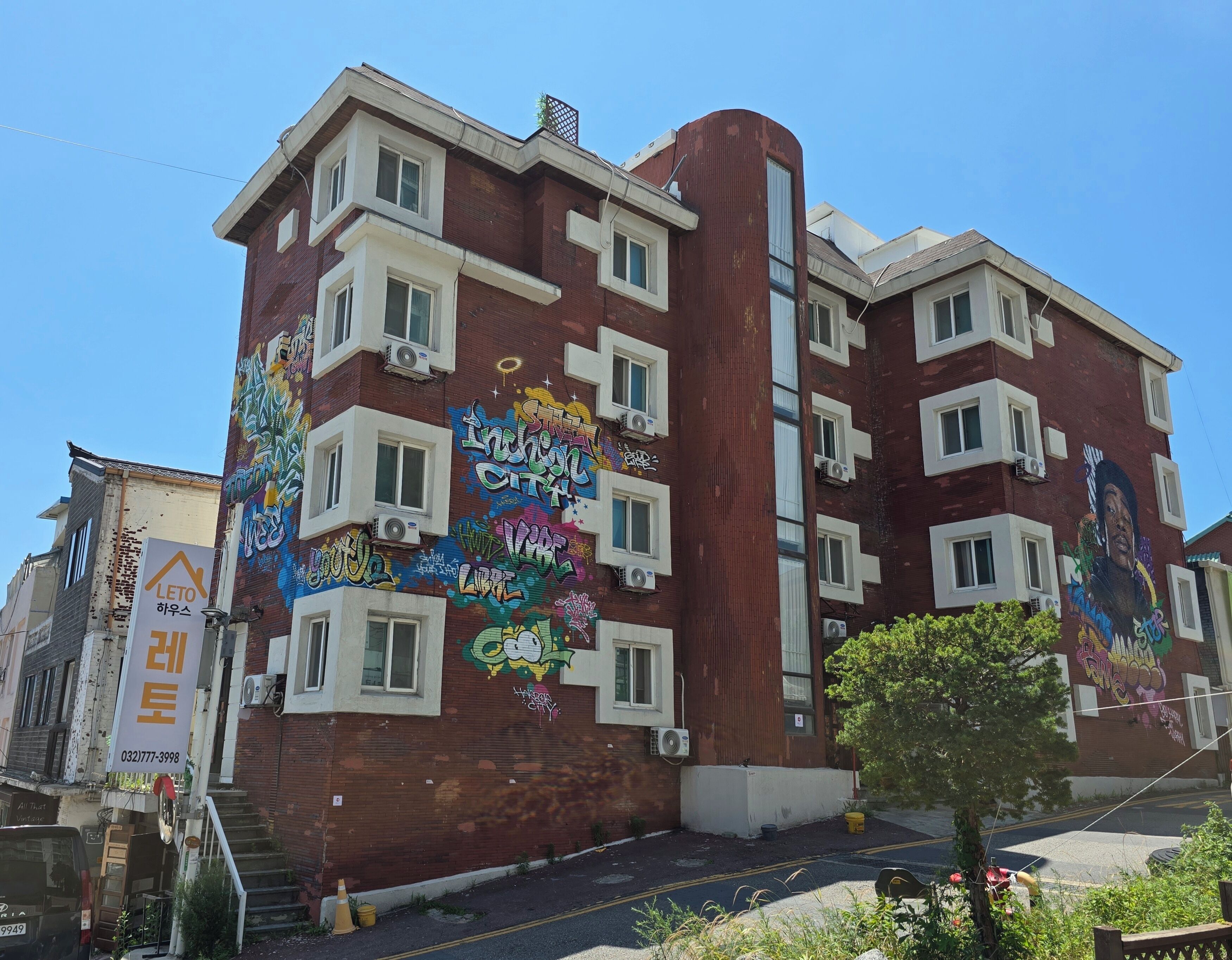 A multi-story building with graffiti art on the exterior walls, air conditioning units, and a sign with Korean text.