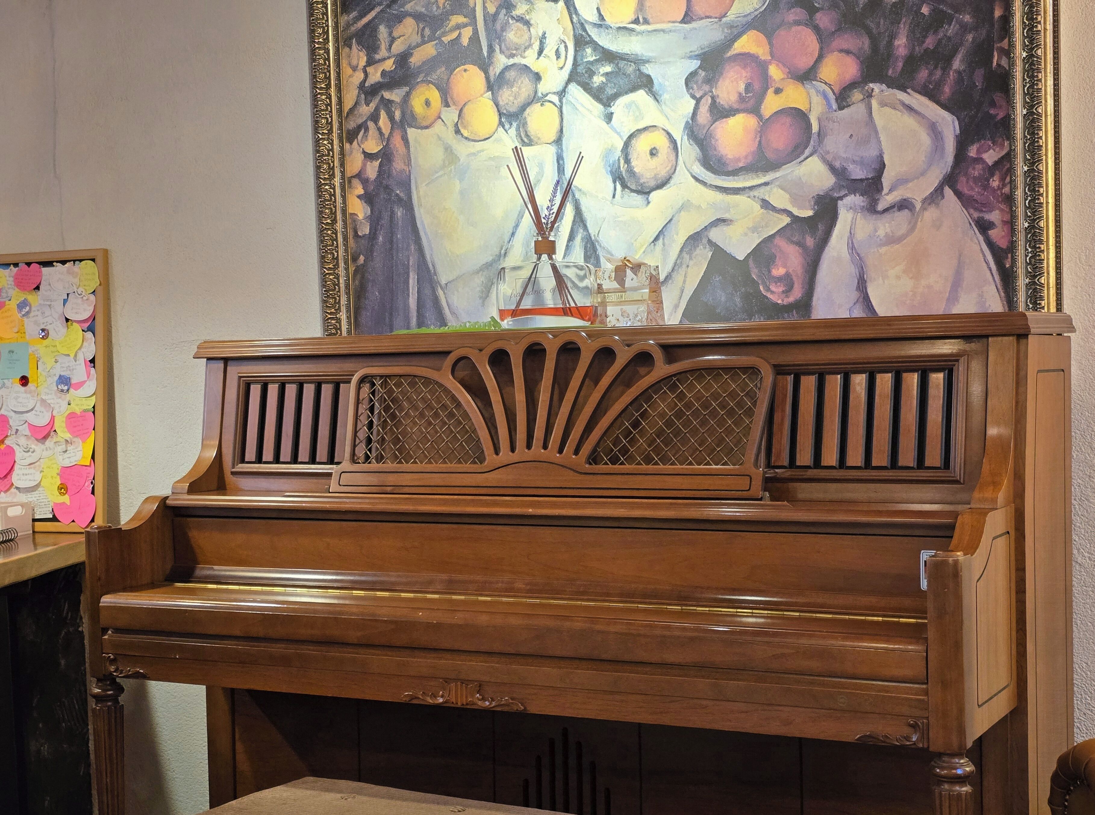 A wooden piano with a decorative front panel and a painting of fruit above it.