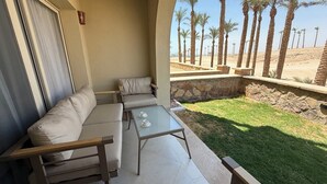 Un balcón con sofá, una mesa de vidrio y vistas a palmeras y un paisaje desértico.