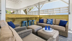 Een overdekt terras met rieten meubels, blauwe krukken en een houten terras.