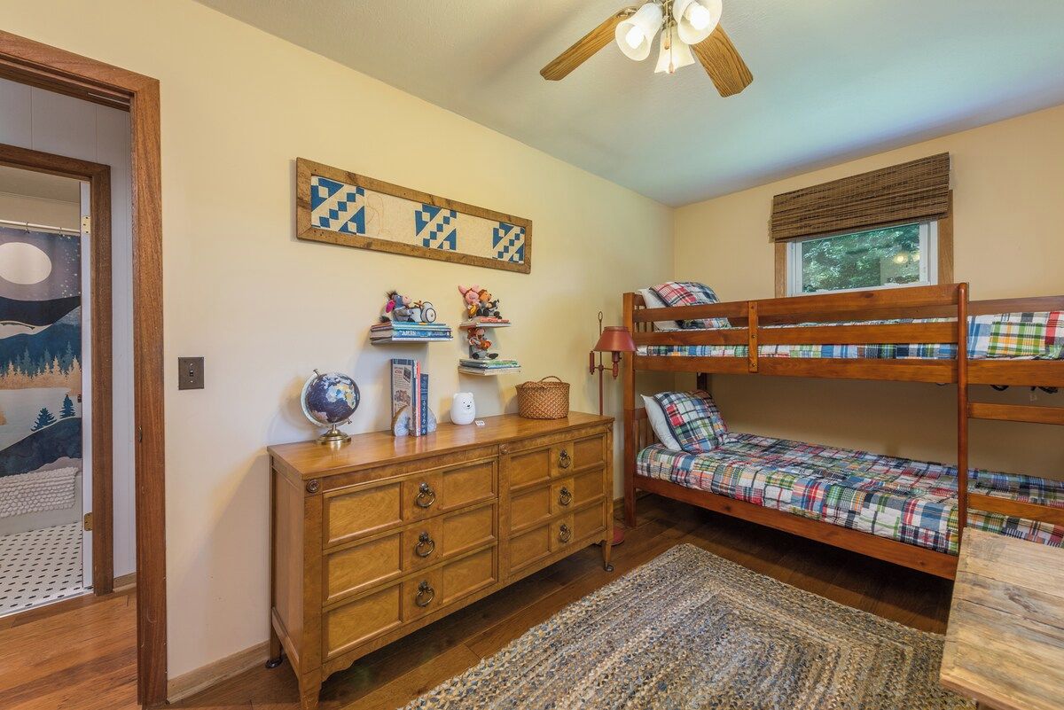 Une chambre d’enfant avec des lits superposés, une commode en bois, un globe terrestre et un élément décoratif mural.