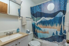 Ein Badezimmer mit Waschbecken, Toilette und Duschvorhang mit einer Nachtszene, die Sterne und Berge zeigt.