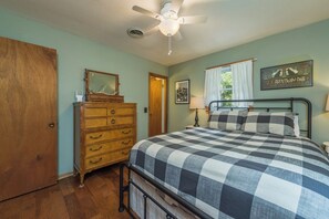 Ein Schlafzimmer mit Bett, Kommode, Deckenventilator und einem Fenster mit Vorhängen.
