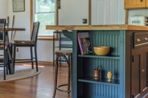 A kitchen with a wooden countertop, a blue cabinet with shelves, and a chair.