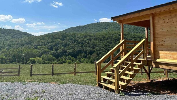 Una cabaña de madera con una escalera que lleva a un porche cubierto, rodeada por un área de grava y una valla de madera.