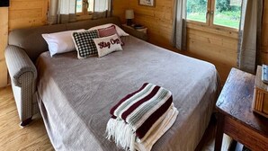 Un dormitorio de cabaña de madera con cama, ventilador de techo y ventana con cortinas.