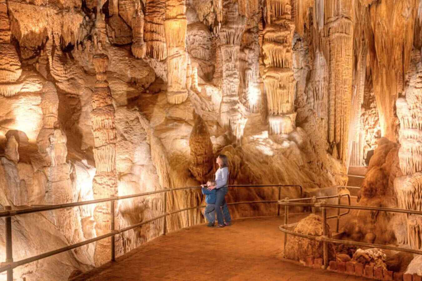 A cave with stalactites and stalagmites, a person standing on a platform, and a railing.