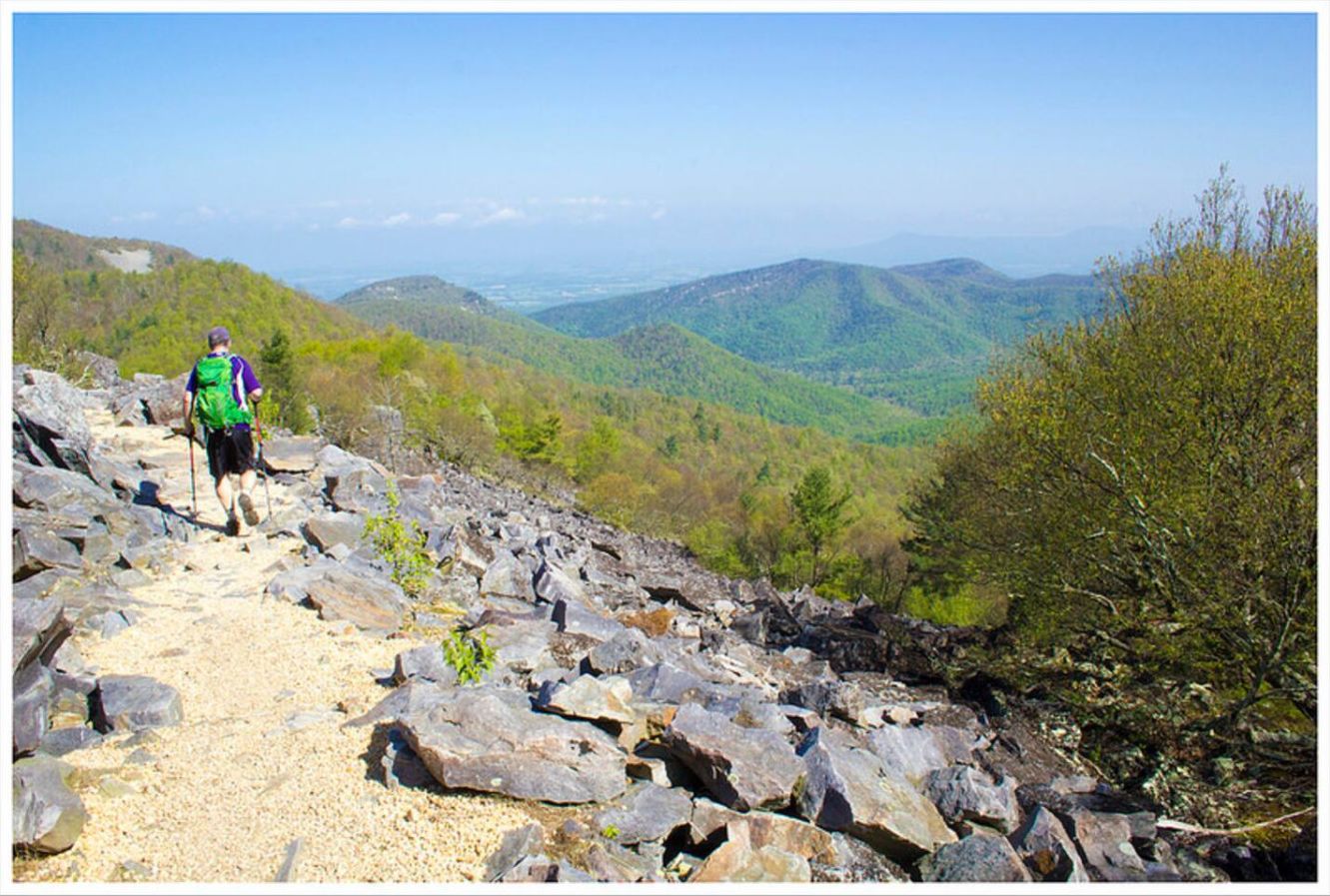 A hiker on a rocky trail with a view of distant mountains.