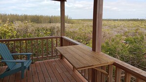 A wooden deck with a table and chairs, overlooking a natural landscape. - Cocolobba Cottage by the Sea in Whale Point (Upper Bogue)