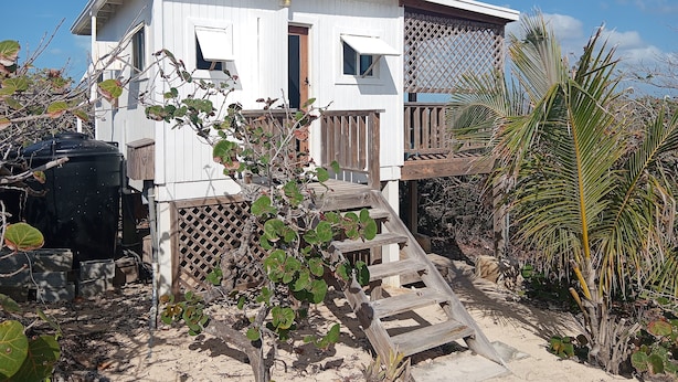 A white two-story house with a wooden deck and a small staircase leading to the entrance. - Cocolobba Cottage by the Sea in Whale Point (Upper Bogue)