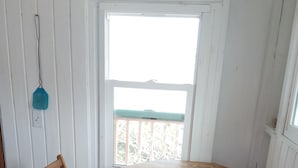 A small dining area with a wooden table and two chairs, a window with a view, and a hanging light fixture. - Cocolobba Cottage by the Sea in Whale Point (Upper Bogue)