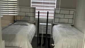 Une chambre avec deux lits, une fenêtre avec des stores et une table de chevet.