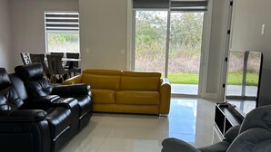 Un vaste salon comprenant un canapé jaune, des canapés en cuir noir et un fauteuil gris.