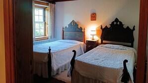 Een kamer met twee houten bedden, een raam met gordijnen, een wandlamp en een klein schilderij.