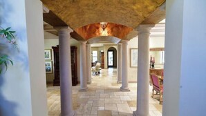 Un intérieur spacieux avec un plafond haut, des colonnes et une vue sur une autre pièce.