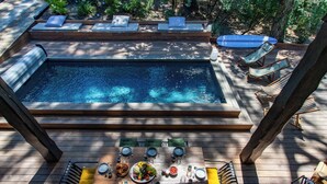 Una terraza de madera con jacuzzi, sillones de descanso y una mesa de comedor lista para una comida.