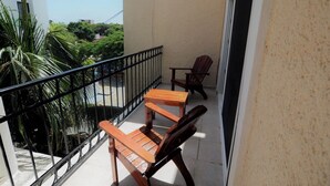 Ein Balkon mit einem Holztisch und zwei Stühlen, einem schwarzen Metallgeländer und Blick auf Grünflächen und Gebäude.