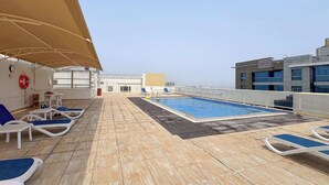 A rooftop pool area with sun loungers and a lifebuoy on the wall. - StayShort - Spacious 2-Bed Al Barsha Escape - Balcony & Modern Amenities, Fits 4 (Al Barsha 1)