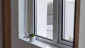 Ein Fenster mit weißem Rahmen, ein kleiner Blumentopf auf der Fensterbank und Blick auf ein Gebäude.