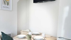 Ein moderner Essbereich mit einem runden Tisch, weißen Stühlen und einem an der Wand befestigten Flachbildfernseher.