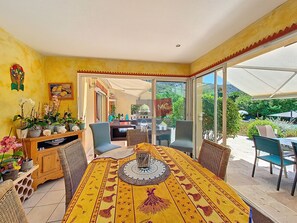 A dining area with a yellow tablecloth, wicker chairs, and a view of the outdoors. - VILLA LES GOONYS (Le Plan-de-la-Tour)